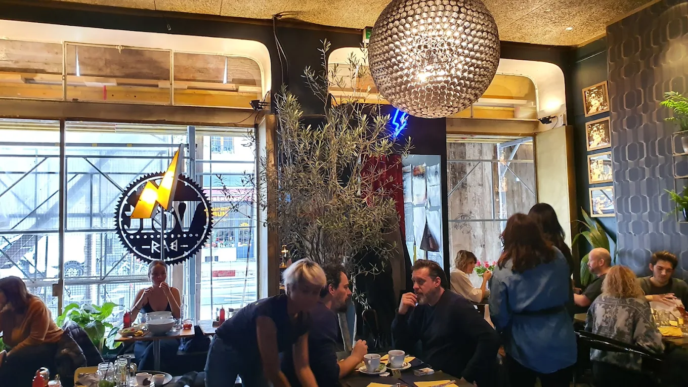 Salle du Volt Bar à Genève : grande boule à facettes, olivier, plantes et clients attablés.